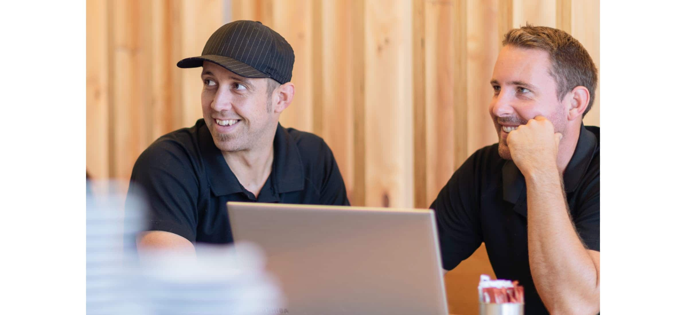 Volare owners Ed and Ryan sitting in front of a laptop smiling.